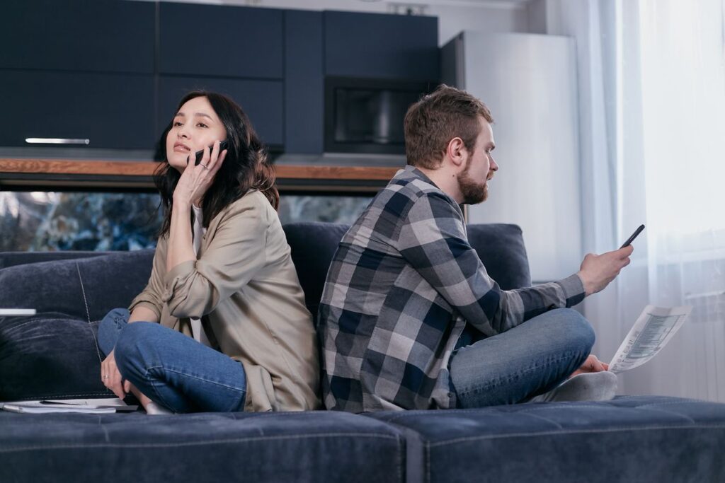 couple experiencing tension sitting with their backs to each other on a blue couch both on their phones